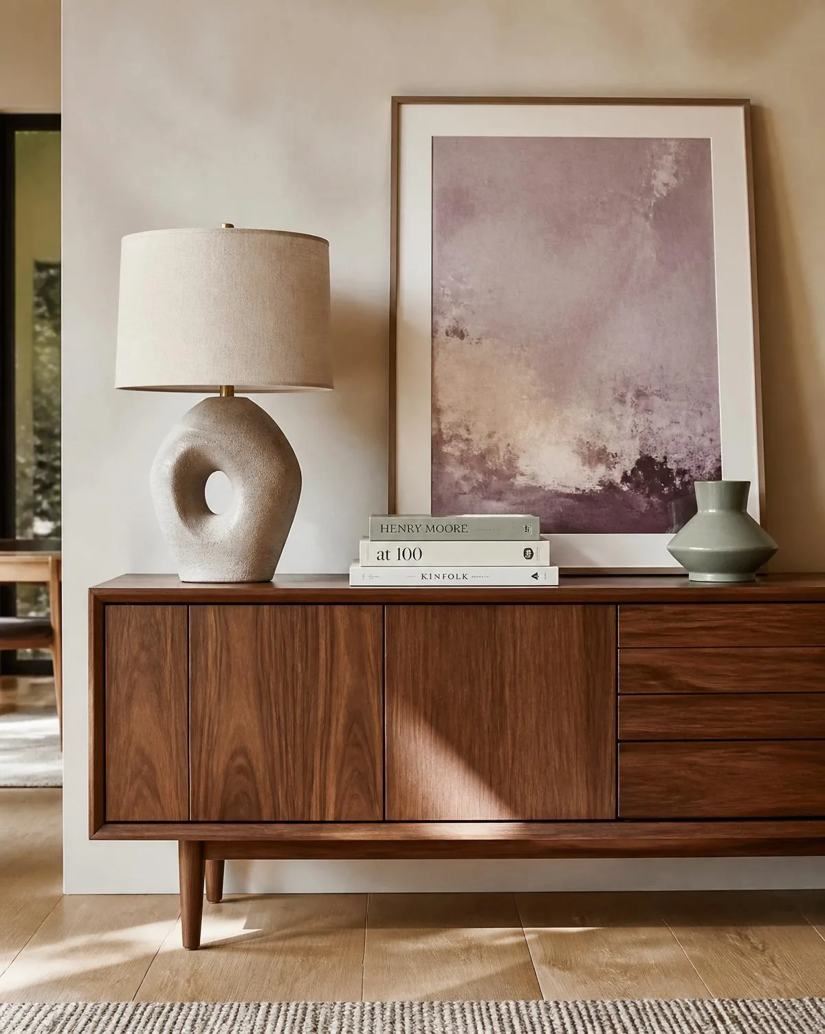 Walnut sideboard styled with a sculptural ceramic lamp, muted abstract artwork and design books